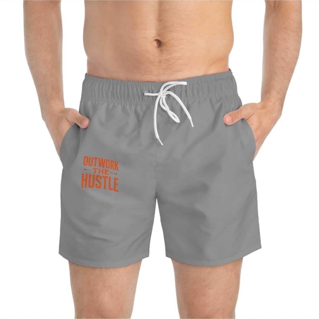 Outwork The Hustle Swim Trunks displayed on a model, featuring a grey color and vibrant orange logo.